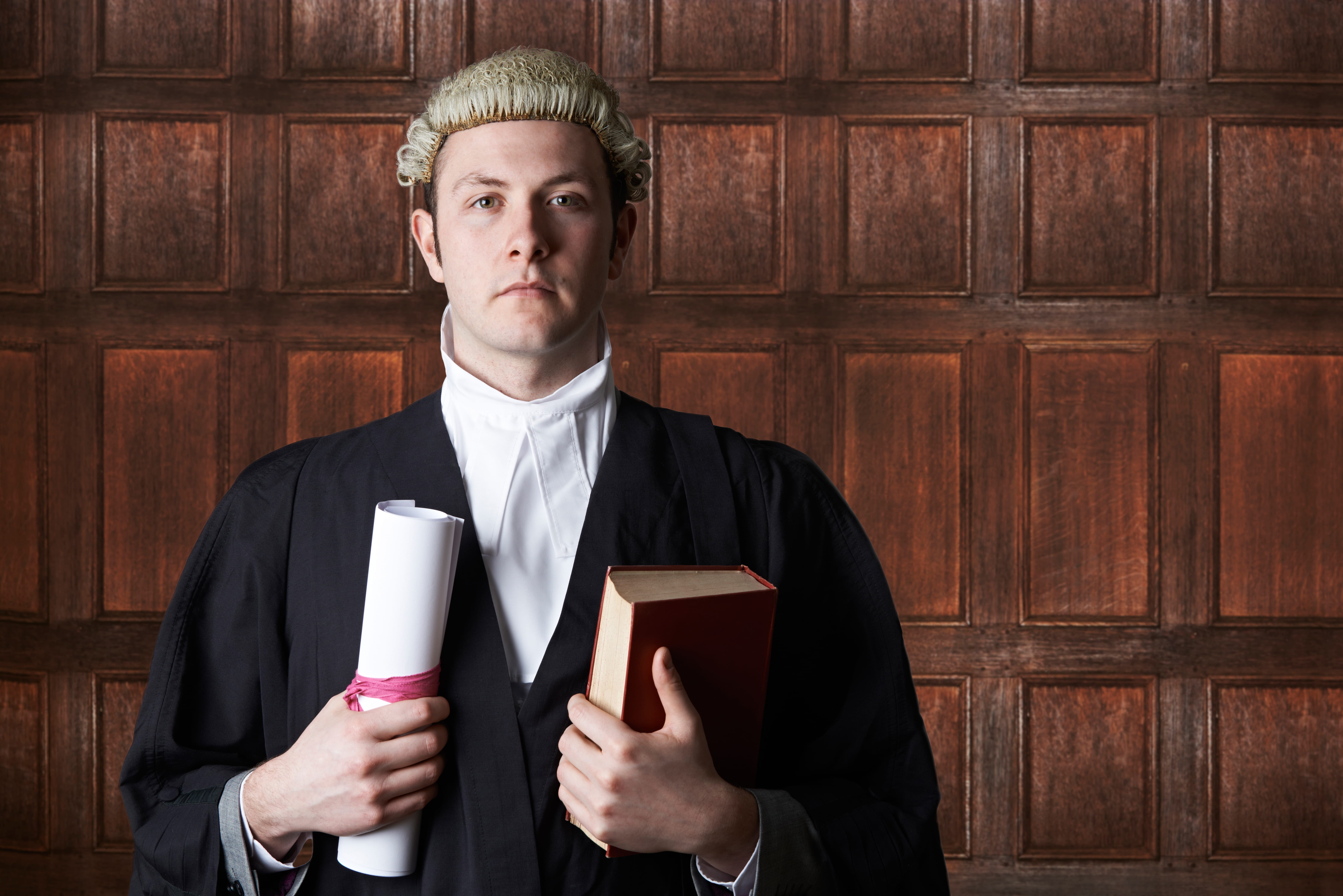 A picture of a white man wearing a tabard and a wig and holding a book and a diploma