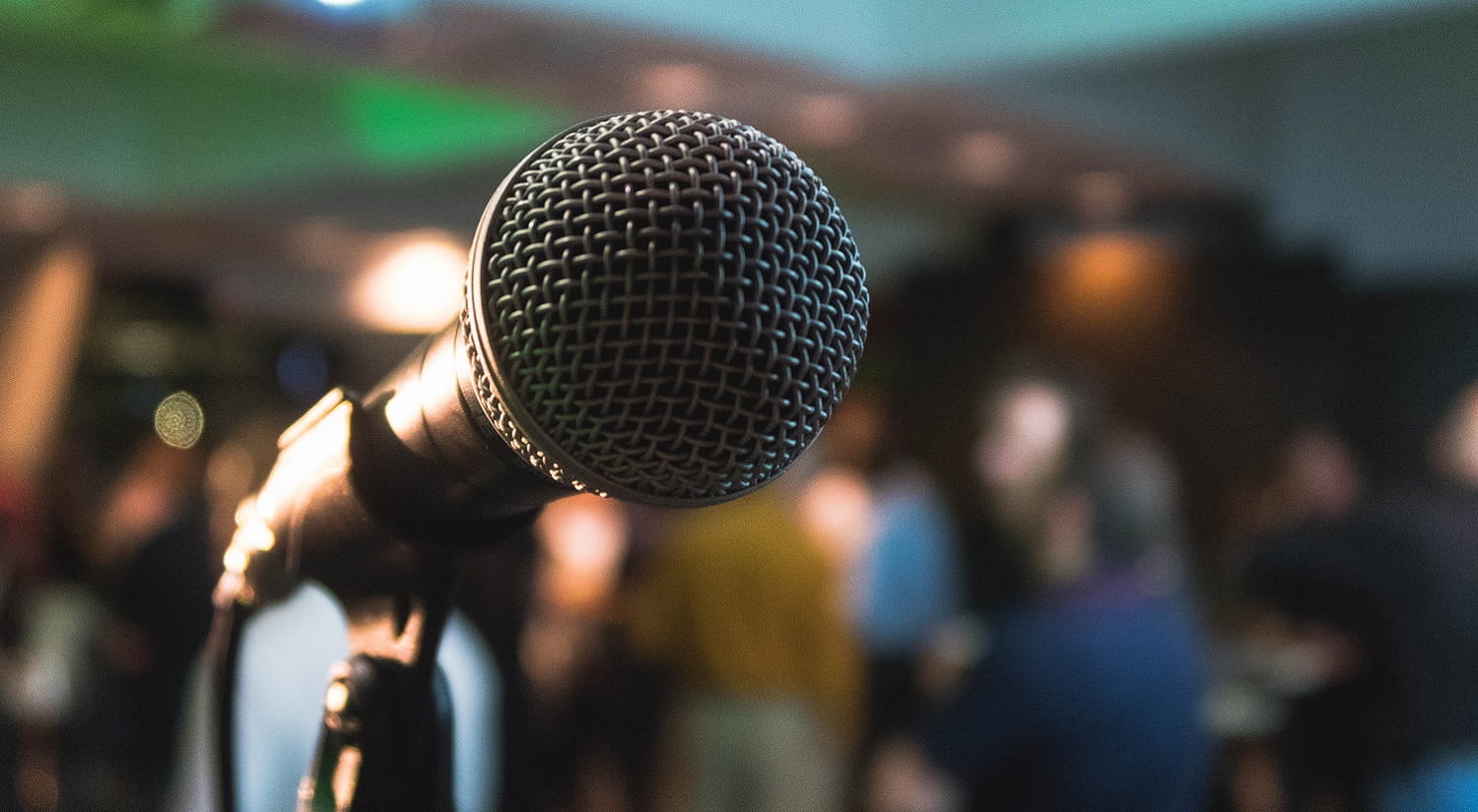A close up of a microphone with a blurred crowded room in the background.