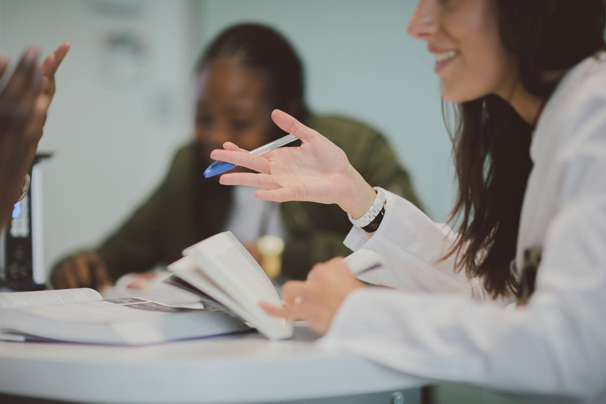 Camera focused on the table over which one woman in the foreground is engaging in conversation and the other woman in the background is taking notes