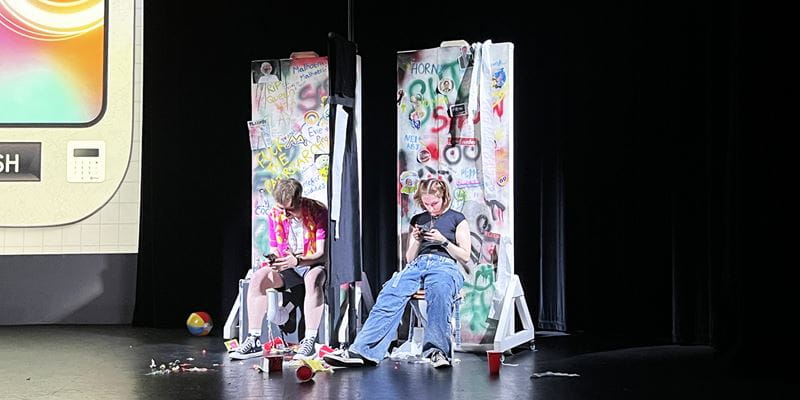 Ethan and Eve sit on the floor of the main stage of the Lakeside Theatre pretending to be sitting on toilets as part of the set for their show "Byte Me".