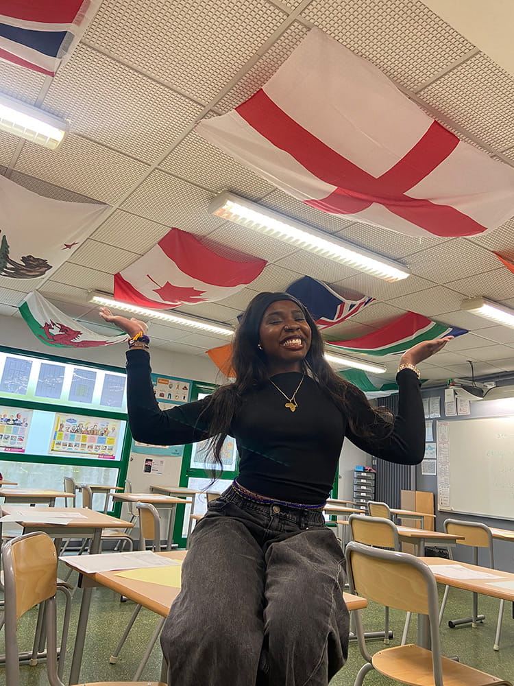 Image of student Eniola Abdul sitting on a table and smiling with lots of national flags above her head