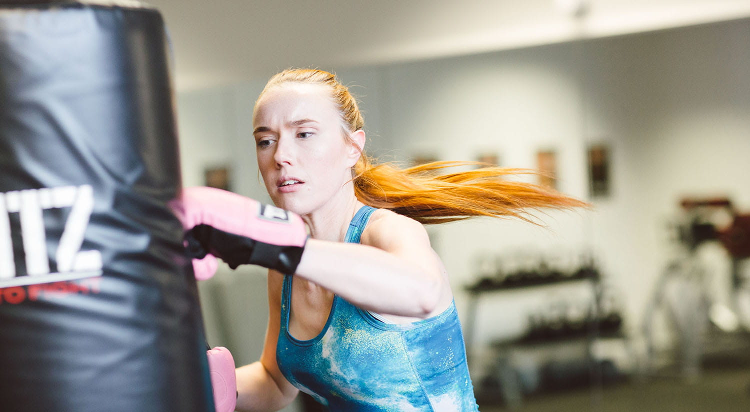 Female student wearing boxing gloves hitting a punch bag 