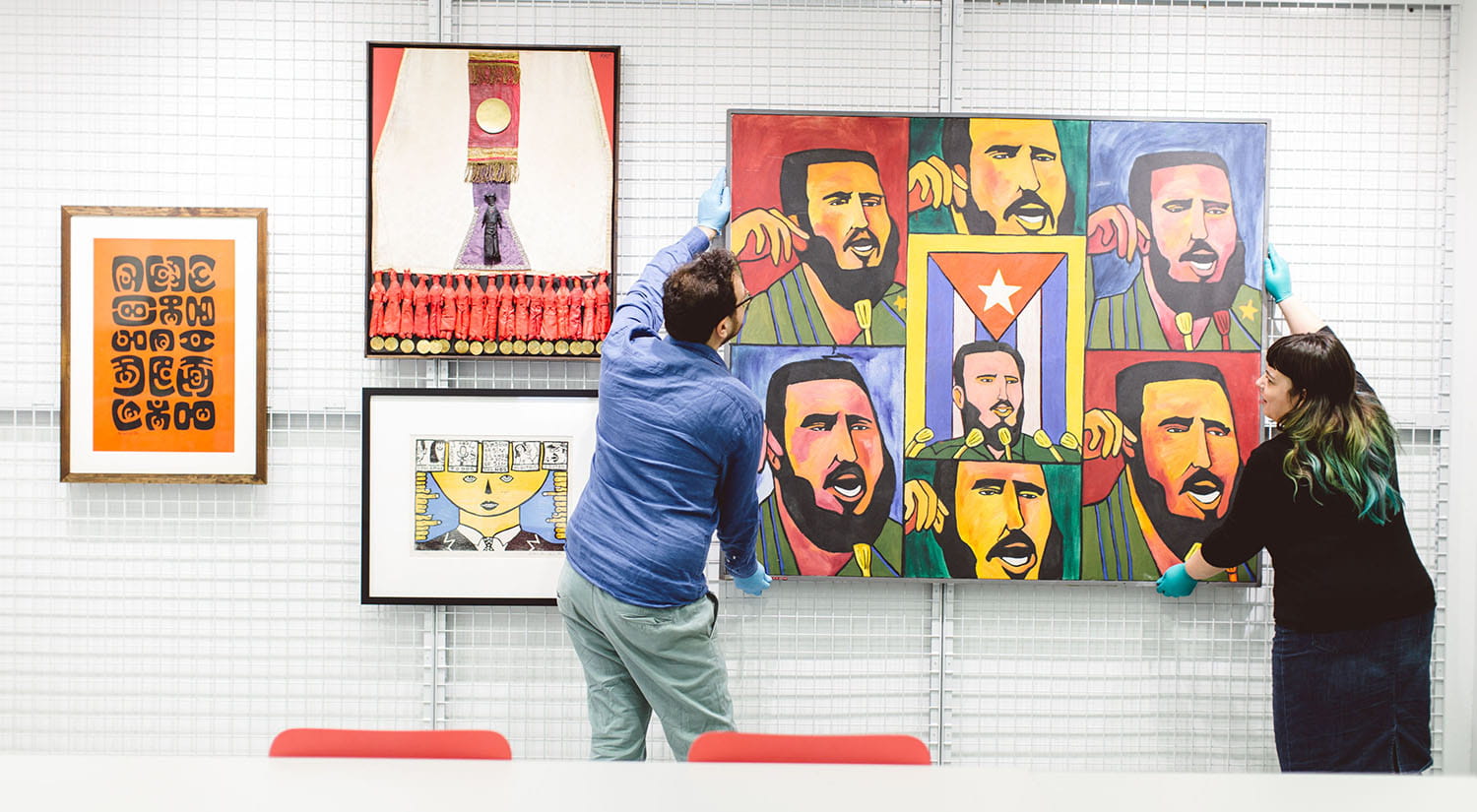 A man and a woman hanging a colourful piece of art on an art gallery wall