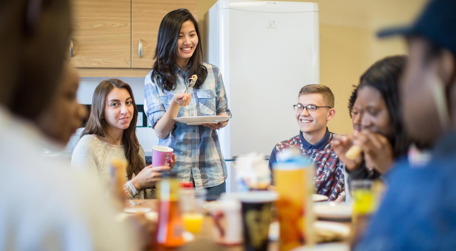 Students chatting and eating in the kitchen.